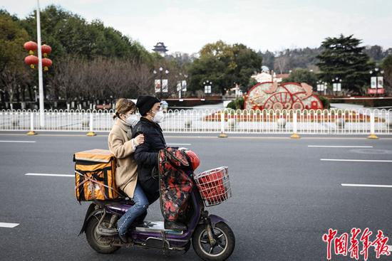 2月29日，武汉市，一对年轻男女驾驶着送外卖的电动车驶过。中青报·中青网记者 赵迪/摄